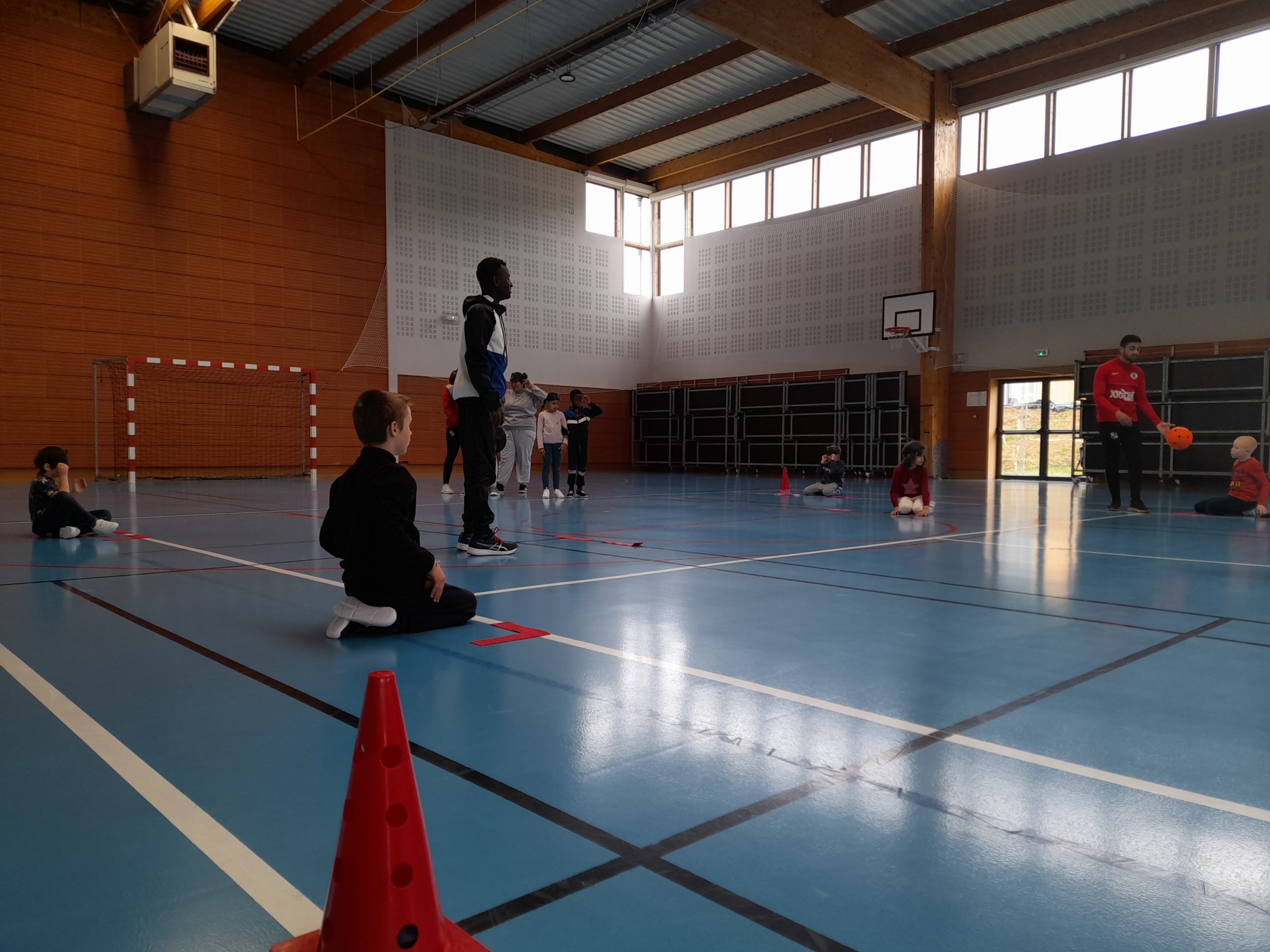 Des jeunes dans un gymnsae écoutent l'éducateur